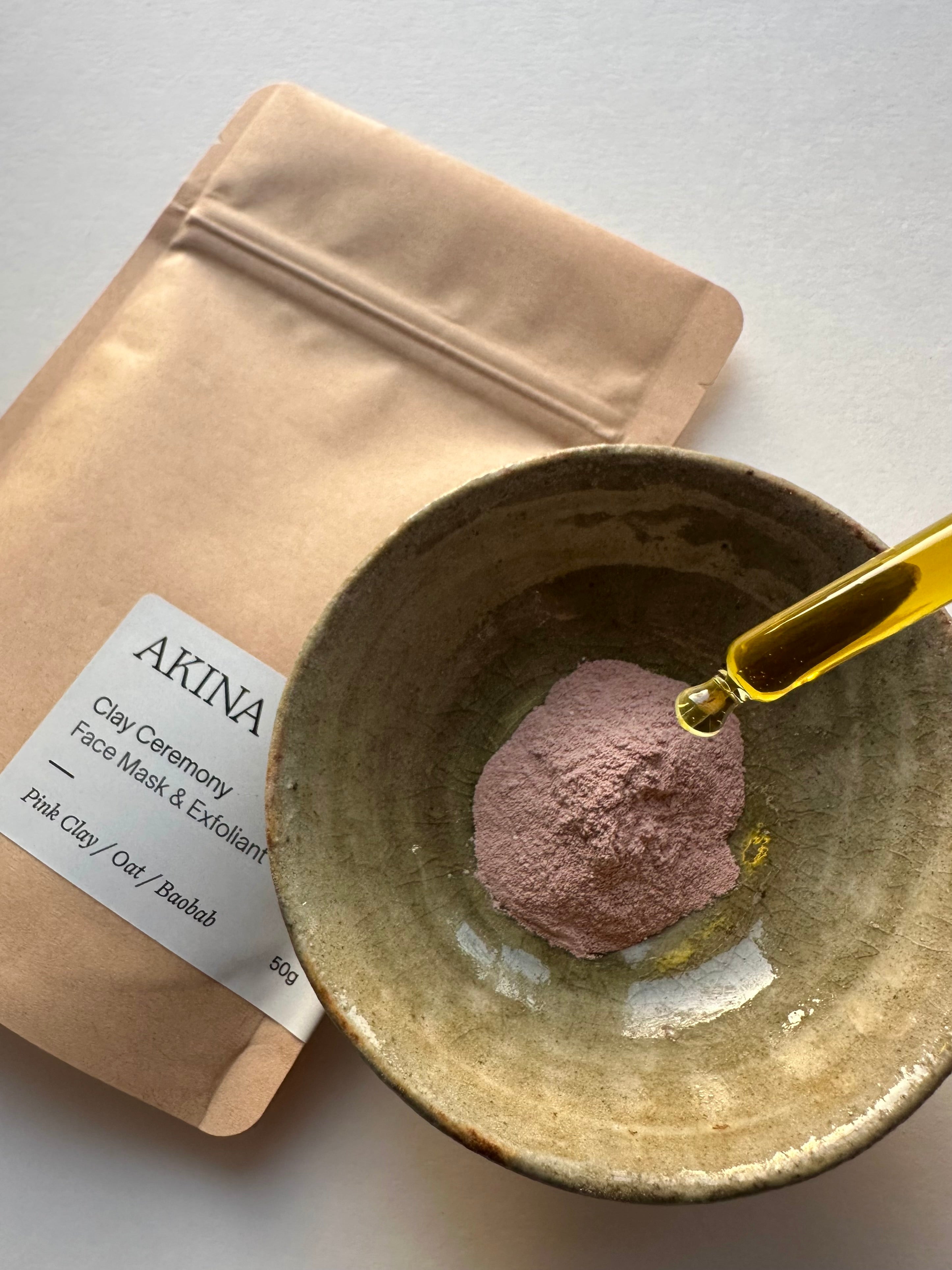 AKINA Clay Ceremony powder mask in a bowl with face oil, preparing a botanical clay treatment